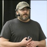 Passport photo of Matt Bacak wearing a dark T-shirt, a khaki cup and a headphone